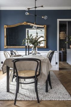 a dining room with blue walls and white chairs, an ornate mirror above the table