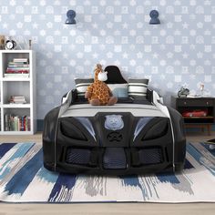 a child's bedroom with blue and white wallpaper, black bedding, and a giraffe stuffed animal