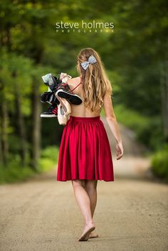 a woman walking down a dirt road holding a pair of shoes and a skateboard