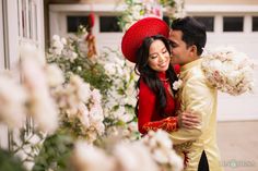 a man and woman standing next to each other in front of white flowers with a red hat on their head