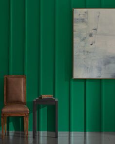 a chair sitting next to a table in front of a green wall with a painting on it