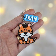 a hand holding a small keychain with an orange and white tiger on it