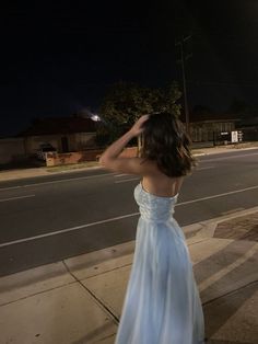 a woman in a blue dress is standing on the sidewalk at night with her hands behind her head