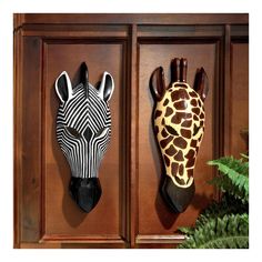 two giraffe head mounted to the side of a wooden wall next to a fern