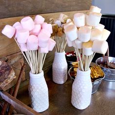 marshmallows are arranged in white vases on a table with other sweets