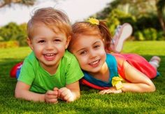 two young children laying on the grass smiling at the camera with their arms around each other