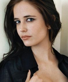 a woman with blue eyes is posing for the camera while wearing a black shirt and holding her hand on her chest