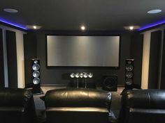 a home theater with black leather chairs and speakers on the wall, in front of an empty screen