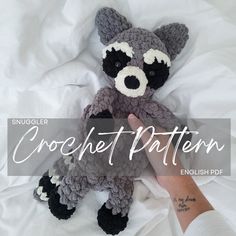 a crocheted raccoon stuffed animal sitting on top of a bed