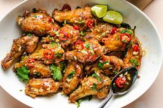 a white bowl filled with chicken wings and garnished with red peppers, cilantro and lime