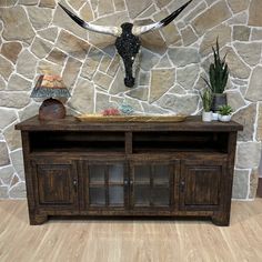 a large wooden cabinet with an animal head on the wall behind it and plants in vases next to it