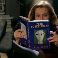 a woman reading from outer space with an alien face on the book in front of her