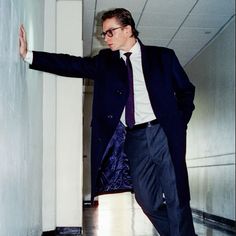 a man in suit and tie leaning against a wall with his hand on the door