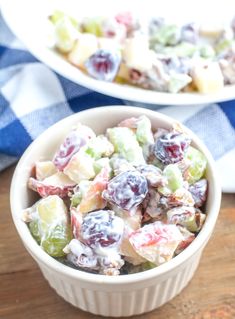 two white bowls filled with fruit salad on top of a wooden table next to a blue and white checkered cloth