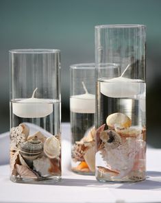 three clear vases filled with seashells and candles