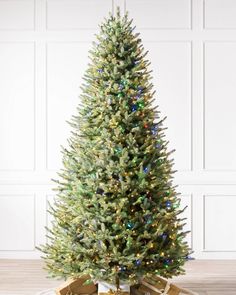 a christmas tree with presents under it in front of a white wall and wooden floor