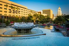 a large fountain in the middle of a park with palm trees and buildings behind it