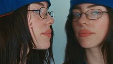 two women wearing baseball caps and glasses are looking at each other's reflection in the mirror