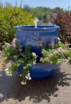 a blue planter filled with lots of flowers next to a body of water in the background