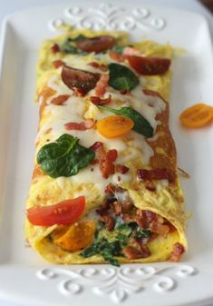 an omelet with bacon, tomatoes and spinach on a white platter