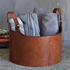 a brown leather basket filled with folded towels and other items sitting on top of a table