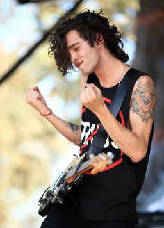 a young man with long hair and tattoos on his arm playing an electric guitar at a music festival