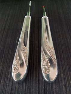 two silver spoons sitting next to each other on a wooden table with flowers in the background