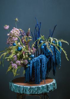 two blue vases filled with flowers on top of a wooden table next to a plant