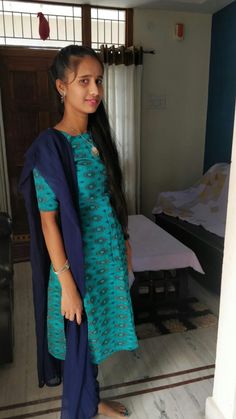 a woman standing in front of a bed wearing a green and blue dress with long sleeves