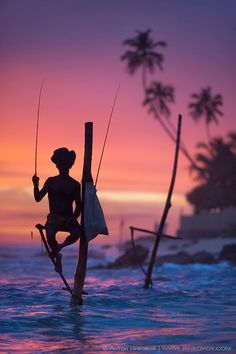 the silhouette of a person standing on a pole in the water with fishing rods and poles