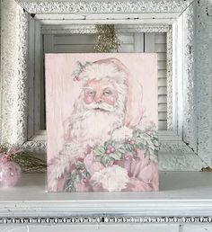 a painting of a santa clause on a white mantle next to a pink ornament