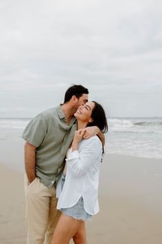 a man and woman are kissing on the beach while standing next to each other with their arms around each other