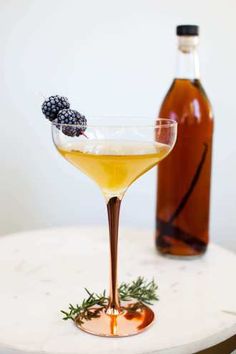 a cocktail in a martini glass with blackberries on the rim next to a bottle