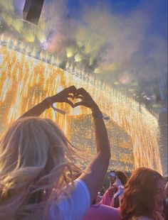 people standing in front of a stage holding their hands up to the sky with fireworks coming from them