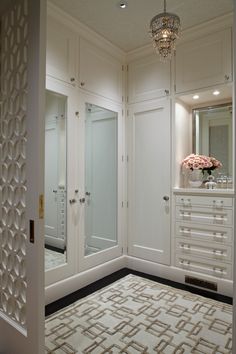 an image of a white closet with mirrors and lights on the doors, in front of a chandelier