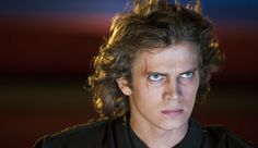 a man with long hair and blue eyes looks at the camera while wearing a black shirt