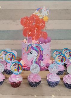 a table topped with lots of cupcakes next to a pink cake and balloons