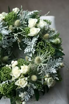 a wreath with white flowers and greenery is displayed on a tableclothed surface