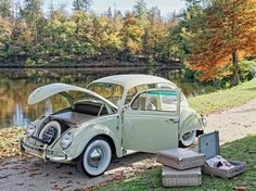 an old car parked next to a lake with its hood open and luggage on the ground