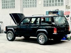 a black suv parked in front of a white brick building with its hood up and the door open