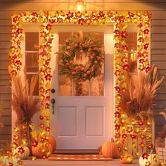 a front porch decorated for fall with pumpkins and flowers on the steps, wreathed door