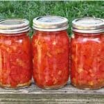 four jars filled with pickles sitting on top of a wooden table next to grass