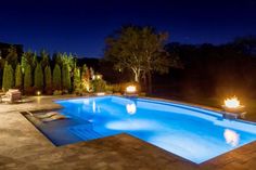 an outdoor swimming pool lit up at night with firepits in the back ground