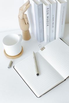 a white desk with a pen, coffee cup and books on it next to a stack of books