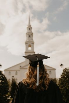 a woman wearing a graduation cap and gown standing in front of a building with a steeple