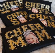 three black shirts with gold letters and pictures of cheer moms on them are laying on a white furnishing