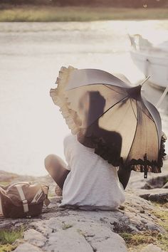 a person sitting on the ground with an umbrella over their head and a boat in the background