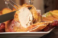 a turkey being cut with a knife on a plate next to other meats and potatoes