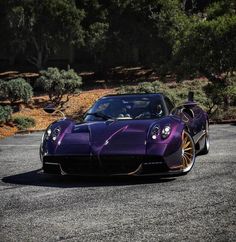 a purple sports car parked in a parking lot next to some bushes and trees on the other side of the road