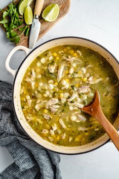 a pot filled with chicken and corn soup on top of a counter next to a cutting board